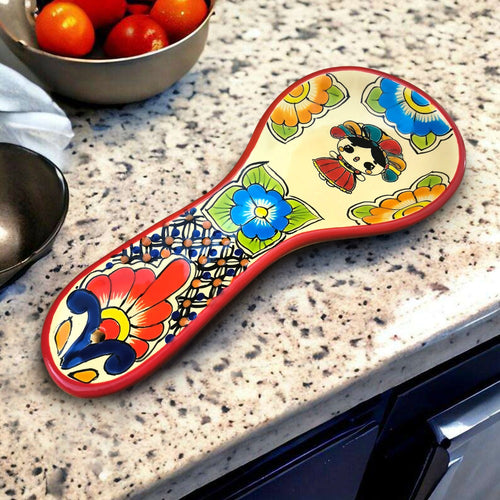 A colorful, hand-painted ceramic spoon rest with a red border featuring floral and geometric patterns, resting on a kitchen counter.